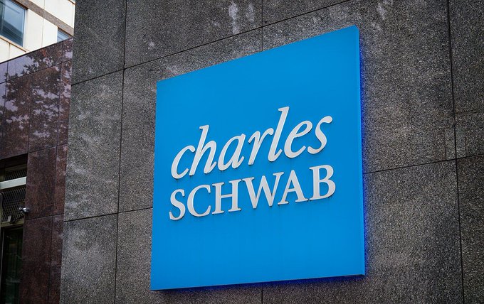 A blue square sign reading 'charles SCHWAB' mounted on a stone building exterior.