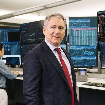 A distinguished middle-aged man in a dark suit and red tie stands confidently in front of multiple trading screens displaying financial charts and market data, suggesting his prominent role in financial markets. The image aligns with the post's theme of Citadel's powerful presence on Wall Street and the competitive, resource-driven nature of the crypto market, though no specific names or tickers are visible.
