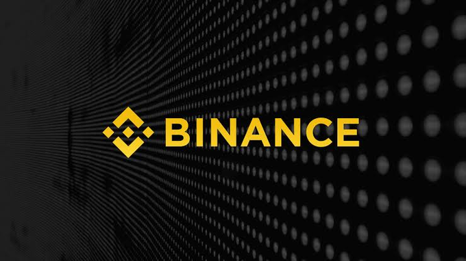 The gold 'BINANCE' logo and its accompanying diamond symbol are displayed against a dark background with a pattern of glowing dots.