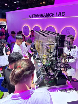 A bustling scene at an 'AI FRAGRANCE LAB' booth where people gather around a robotic machine with multiple nozzles dispensing scents, including a man in a white lab coat demonstrating the equipment.