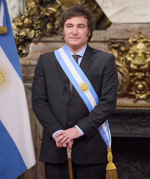 An official portrait of Argentina's President Javier Milei wearing the presidential sash with the Argentine flag visible beside him.