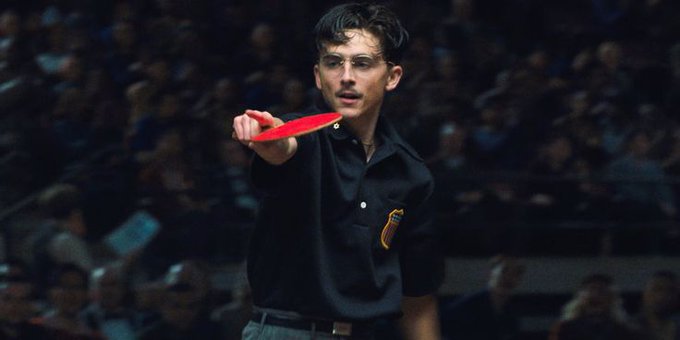The image features a man holding a red frisbee with both hands while standing in front of an audience. The crowd appears to be watching him intently as he prepares to throw the frisbee. The scene suggests that this could be a sports event or a game, and the man is likely participating in it.