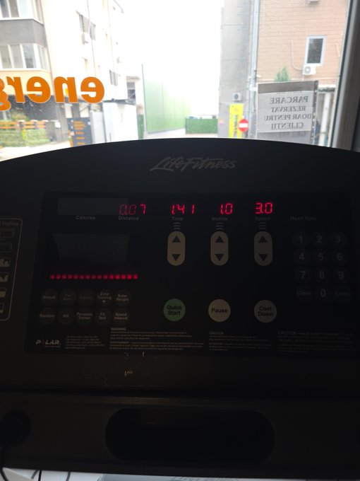 A Life Fitness treadmill control panel is shown mid-workout, displaying 807 calories burned, a distance of 14.1, incline of 10, and a heart rate of 130, with a view of buildings outside the window.
