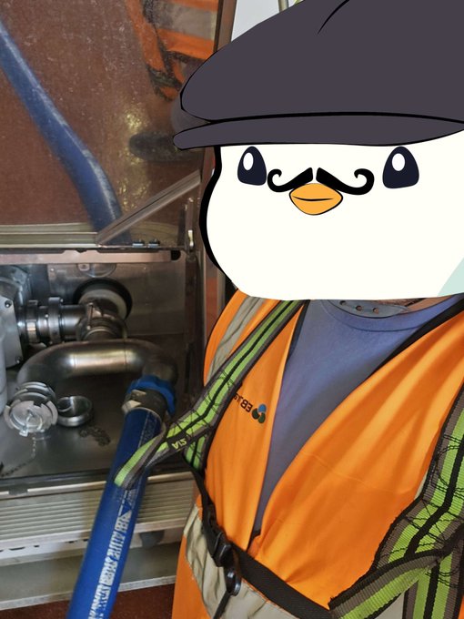A worker in orange safety gear and helmet stands near industrial piping and valves, with a cartoon bird face (similar to a social media avatar) overlaid on top.