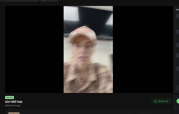 A blurry screenshot from a livestream or video call showing a woman wearing a beige cap and patterned shirt, with text below reading 'Girl Wif Hat' and 'Started 1m ago' alongside a green 'ONLINE' indicator.