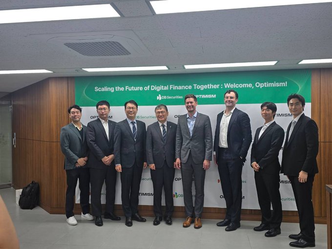 Eight men in business suits pose together in front of a green banner reading 'Scaling the Future of Digital Finance Together: Welcome, Optimism!' with 'CO Securities' and 'OPTIMISM' branding visible.