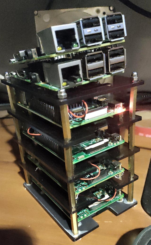 A stacked, multi-tier Raspberry Pi cluster mining rig with network and USB ports visible at the top, illuminated by a red LED, representing the first of a 6-unit cluster mining Monero. The tower houses multiple layered circuit boards connected by wiring, showcasing a custom crypto mining setup.