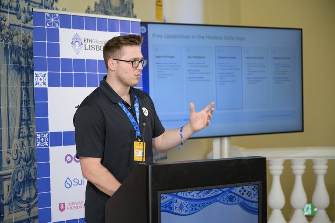 A man wearing glasses and a lanyard speaks at a podium during an 'ETHGlobal LISBOA' event, presenting slides titled 'Five capabilities in the Hedera Skills repo' including Digital ID Plugin, Dex Intelligence, and Application Meter.