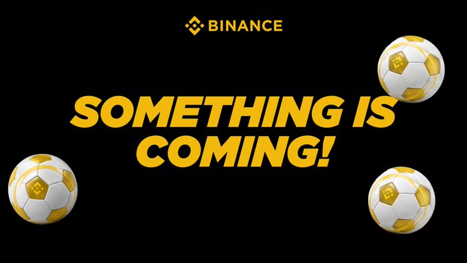 A Binance promotional graphic features the bold yellow text "SOMETHING IS COMING!" against a black background, accented by three gold and white soccer balls that visually reinforce the post's "the game isn't over yet" message, teasing an upcoming announcement in the Binance Discord community.