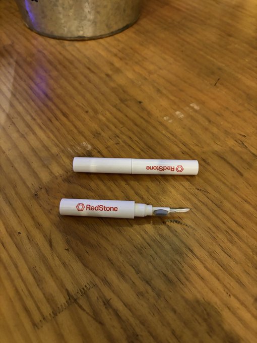 A RedStone branded craft knife or precision tool with its cap beside it, lying on a wooden surface.