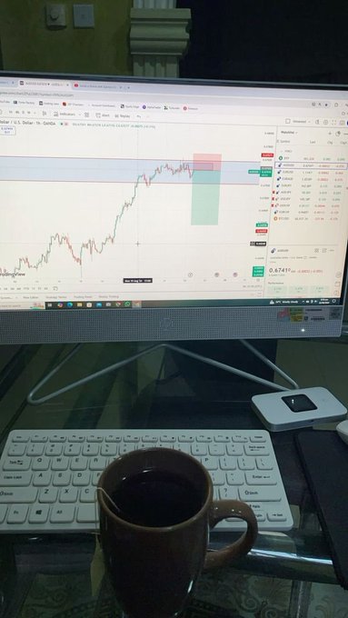 A photograph of a desk setup showing a monitor displaying a TradingView GBP/USD chart, accompanied by a keyboard and a brown coffee mug.