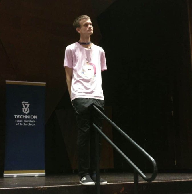 The image features a young man standing on a stage, wearing a pink shirt with a unicorn design. He has his hands behind his back while looking off into the distance. The background of the scene includes a banner that reads "30-40 million zcash no big deal I'm sure they will only spend it ethically and timely like the ETH Foundation". This suggests that there might be an event or gathering related to cryptocurrency, such as a conference or exhibition, where people are discussing and sharing ideas about this digital currency.