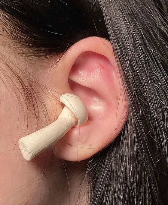 Close-up of an ear wearing a cream-colored, mushroom-shaped ear plug that sits against the earlobe.