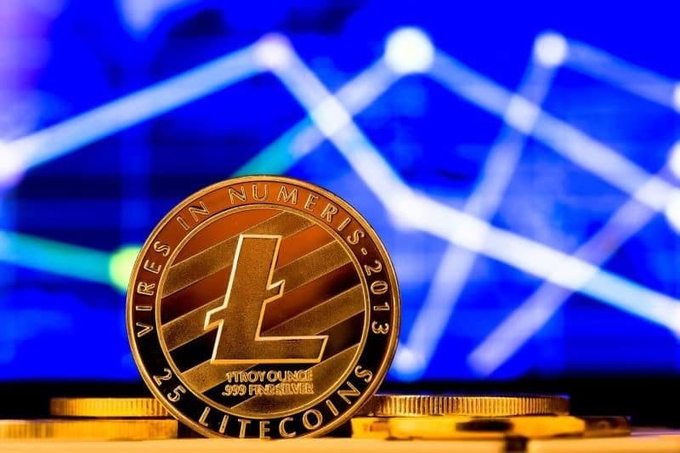 A physical Litecoin (LTC) coin, marked "VIRES IN NUMERIS," "1 TROY OUNCE .999 FINE SILVER," and "2013," stands prominently in the foreground against a blurred blue background of rising chart lines—perfectly capturing the comeback spirit of LTC highlighted in the post.