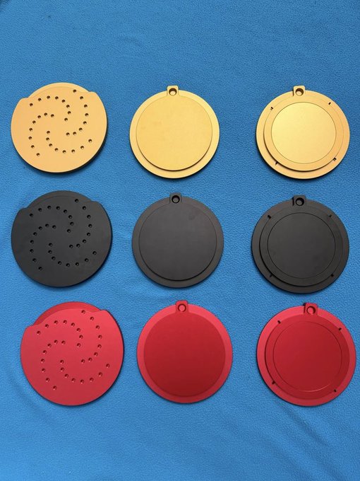 Nine circular objects in three colors (tan, black, and red) are arranged in a grid on a blue surface, featuring designs with holes, cutouts, and small loops.