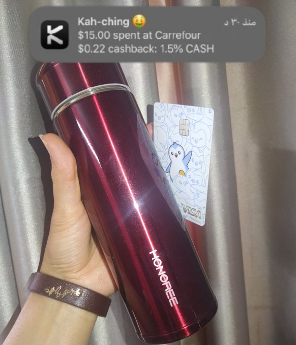 A hand holds a burgundy Honor thermos alongside a Visa card, with a notification showing "$15.00 spent at Carrefour" yielding "$0.22 cashback: 1.5% CASH" on the KAST app, illustrating the small but satisfying crypto cashback reward earned from the purchase.
