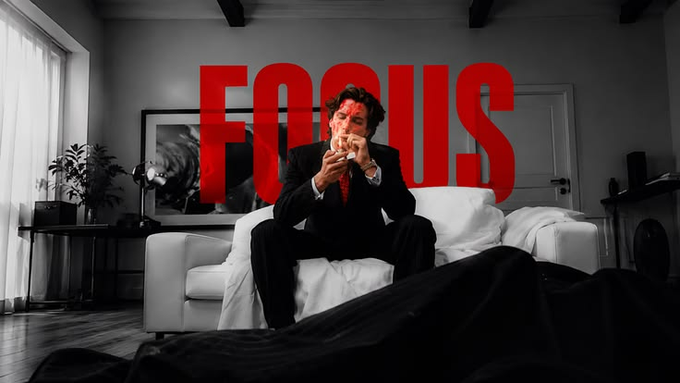 A person in a suit sitting on a couch with blood on their face, with the word "FOCUS" in large red letters in the background.