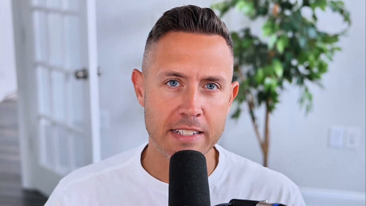 The image shows a man wearing a white shirt holding a microphone, possibly speaking into it or recording a video. The background features a plant and a door, suggesting an indoor setting like a room or studio. There are also several other words visible in the image that seem unrelated to the main subject of the photo.
