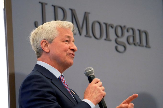 A distinguished man in a navy suit and striped tie speaks into a microphone in front of a large "JPMorgan" logo, likely during a corporate event or press conference. The image visually reinforces the accompanying news about JPMorgan's significant $610 million disclosure regarding a position in BlackRock's spot Bitcoin ETF.