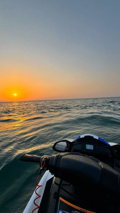 A first-person view from a jet ski gliding across the ocean toward a vibrant sunset on the horizon.