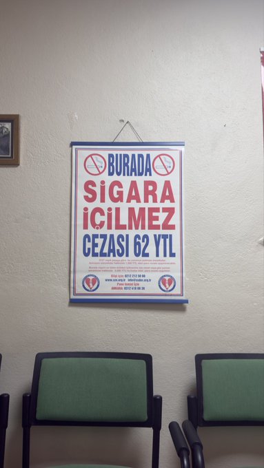 A Turkish no-smoking sign hangs on a white wall above green chairs, reading 'BURADA SİGARA İÇİLMEZ CEZASI 62 YTL' with a fine of 62 YTL.