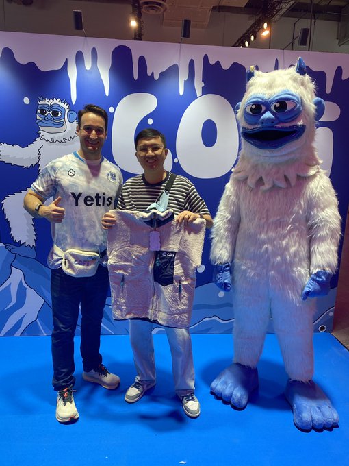 Two men standing with a yeti mascot at what appears to be a 'GOALI' event, one holding up a jersey with the name 'C.601'.