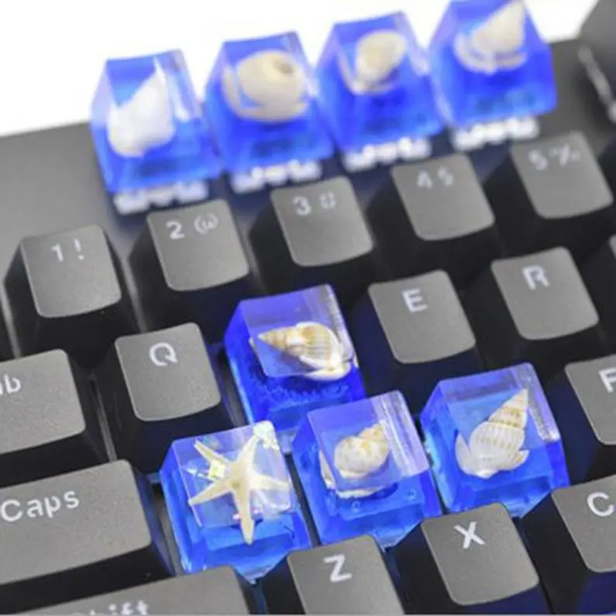 A close-up of a mechanical keyboard featuring custom translucent blue keycaps embedded with real seashells and a starfish.