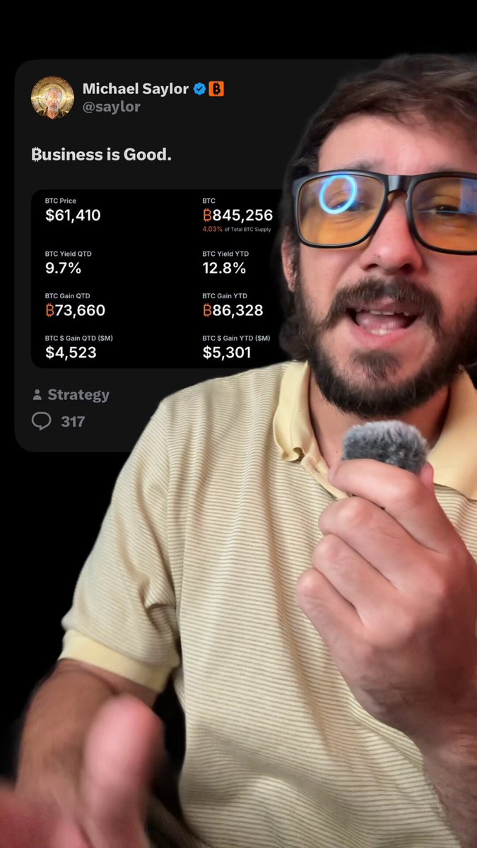 The image shows a man sitting down while wearing glasses and holding a microphone. He has his hand placed over his mouth as if giving a speech, possibly related to investing or business trends. The background features text which talks about Bitcoin, with the caption "Why is Michael Saylor saying business is good despite bitcoin's losses? Because MSTR is built on Bitcoin not fiat. Meaning the more Bitcoin they have, the closer they are to their goals." This could be a reference to the man holding up a microphone, possibly for an interview or a public speaking event about his perspective on investing in Bitcoin and cryptocurrency.