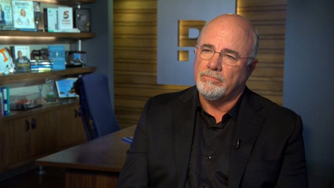 A bald man with glasses and a grey beard wearing a dark suit jacket sits in what appears to be an office setting during an interview.