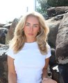 A blonde woman in a white top poses outdoors among large rocks, presumably the subject referenced in the post about Bonnie Blue's controversial child-naming auction and its various bidders.