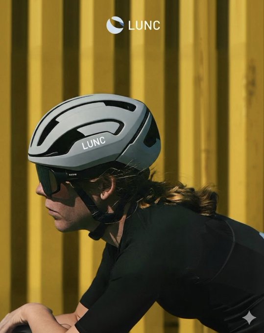 A cyclist wearing a white LUNC helmet and sunglasses is photographed in profile against a yellow corrugated metal wall, with the LUNC brand logo displayed at the top.