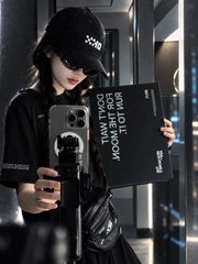 A selfie of a person wearing a black cap with 'XOXO' written on it, holding a phone and a book that reads 'HOW TO DEAL WITH HATERS IN NEW NORMAL ERA' and 'INFINITE SKY'.