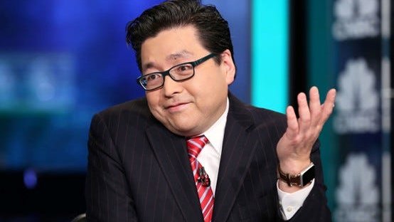 A man wearing a dark pinstripe suit, red striped tie, and glasses gestures with his hand while speaking in what appears to be a television studio setting.