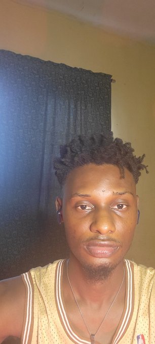 A close-up selfie of a young man with short dreadlocks, a small goatee, and a basketball jersey.