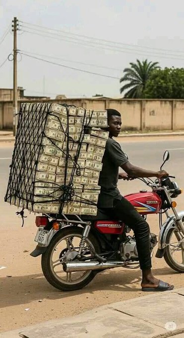 A man rides a motorcycle loaded with a massive cargo of bundled cash strapped to a metal frame on the back, traveling along a road with a palm tree in the background.