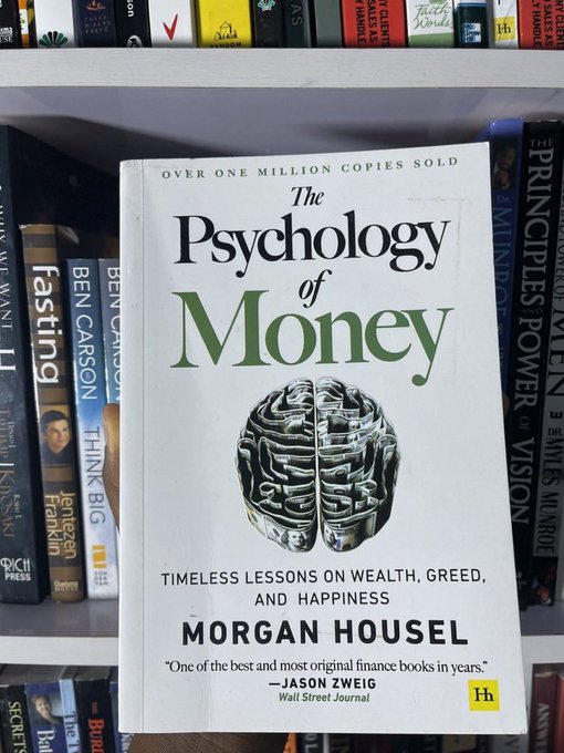 A copy of the book 'The Psychology of Money: Timeless Lessons on Wealth, Greed, and Happiness' by Morgan Housel displayed on a bookshelf, noting 'Over One Million Copies Sold' and a quote from Jason Zweig of the Wall Street Journal.