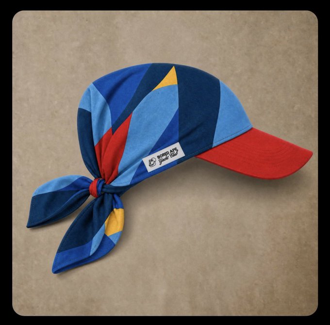 A colorful bandana-style cap with blue, red, and yellow geometric patterns and a tied tail at the back, featuring a red brim and a "BORED APE Yacht Club" label, fitting the playful, festive vibe of Pride celebrations suggested by the post.