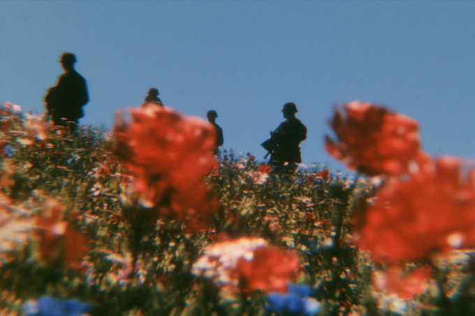 Silhouetted figures stand atop a hillside beyond a blurred foreground of vibrant red and pink wildflowers beneath a clear blue sky. The image pairs with the post by evoking a quiet, networked gathering on shared ground—"common ground" rendered literally as a field where scattered silhouettes pause on the horizon.