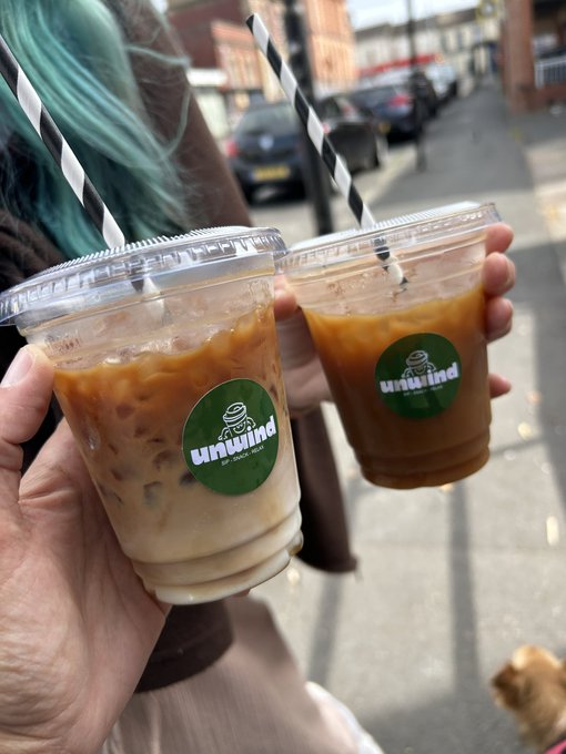 Two people holding iced coffee drinks from a shop called 'Unwind' in clear plastic cups with black and white striped straws.
