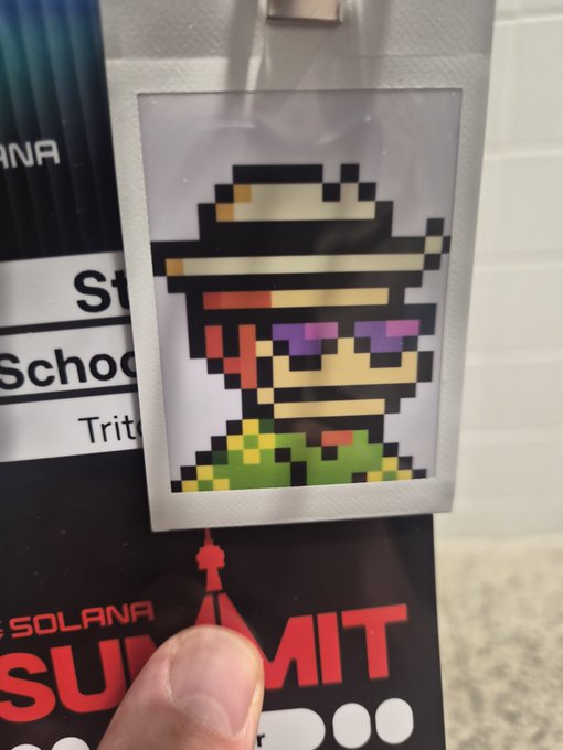 A photo of a Solana Summit badge featuring pixel art of a character wearing a sombrero and purple sunglasses, attached to a lanyard held by a person's hand.