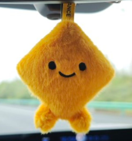 A cute, smiling plush yellow star-shaped character hanging from a car's rearview mirror.