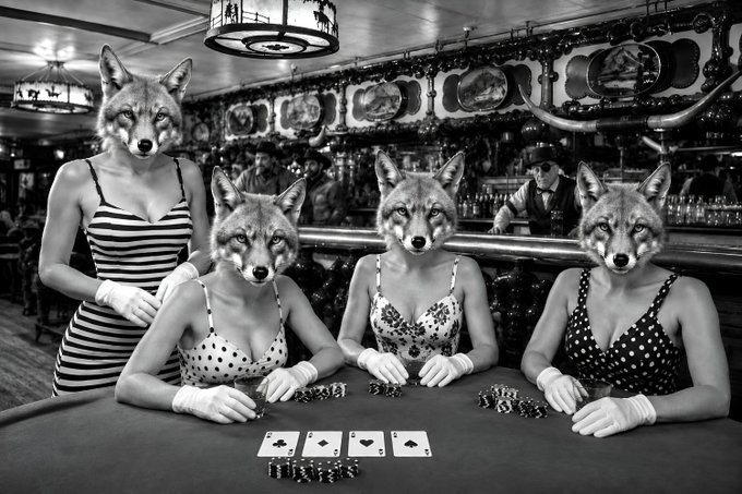 A surreal black-and-white photograph of four women in vintage polka-dot and striped dresses seated at a casino card table, each with a wolf's head instead of a human face, with playing cards and chips before them.