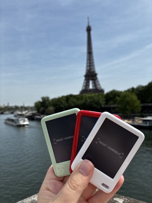 A hand holds three small devices displaying "TRUST YOURSELF" in green, red, and white, posed in front of the Eiffel Tower. The "choose your fighter" caption plays on the trio of devices as colorful "fighters," each in a different hue ready to be picked.