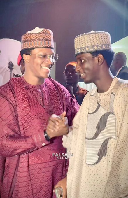 Two men in traditional Nigerian attire smile warmly while shaking hands at what appears to be a wedding dinner, with a "FALSA MEDIA" watermark visible at the bottom of the image, illustrating the social gathering where crypto influencer @ahmedxm01 presented @YahayaCrypto with a $10,000 (approximately ₦14 million) wedding gift.
