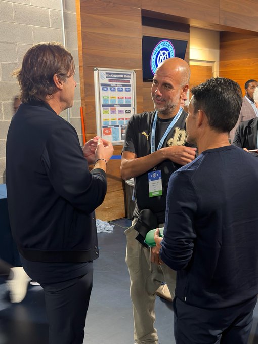 Pep Guardiola chats with Mauricio Pochettino and another man in a concourse featuring a "New York City FC" logo on the wall, ahead of NYCFC's match against the Red Bulls. A "2023 Conference Standings" board is visible in the background.