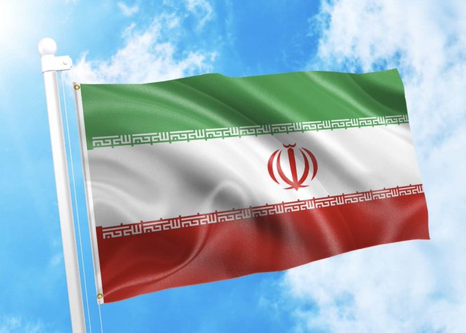The flag of Iran waves against a blue, cloudy sky, visually representing the country at the center of the report. The image illustrates the Iranian backdrop to the Reuters investigation into a $4 billion crypto pipeline processed through an unlicensed Dubai exchange since May 2024.