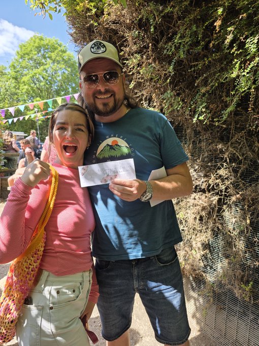 A man and woman celebrate joyfully outdoors, with the man wearing a "World" t-shirt and cap, as the woman excitedly displays what appears to be a winning ticket in her hand—perfectly capturing the "GM World" and "#winning" spirit of the post.