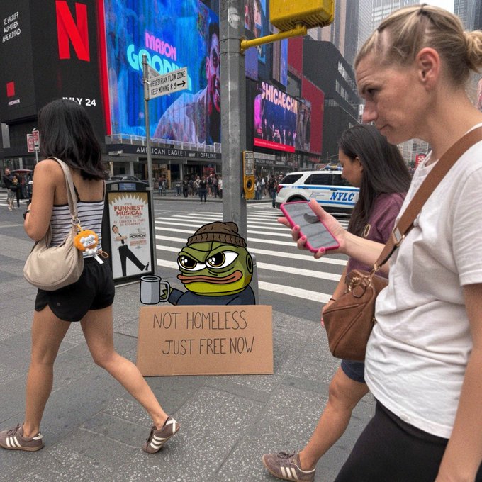 A Pepe the Frog meme is digitally placed into a New York City street scene with a cardboard sign reading 'NOT HOMELESS JUST FREE NOW,' set against Times Square billboards.