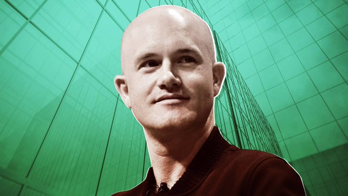 A close-up of a bald man with a slight smile wearing a dark shirt, set against a bright green modern building background.