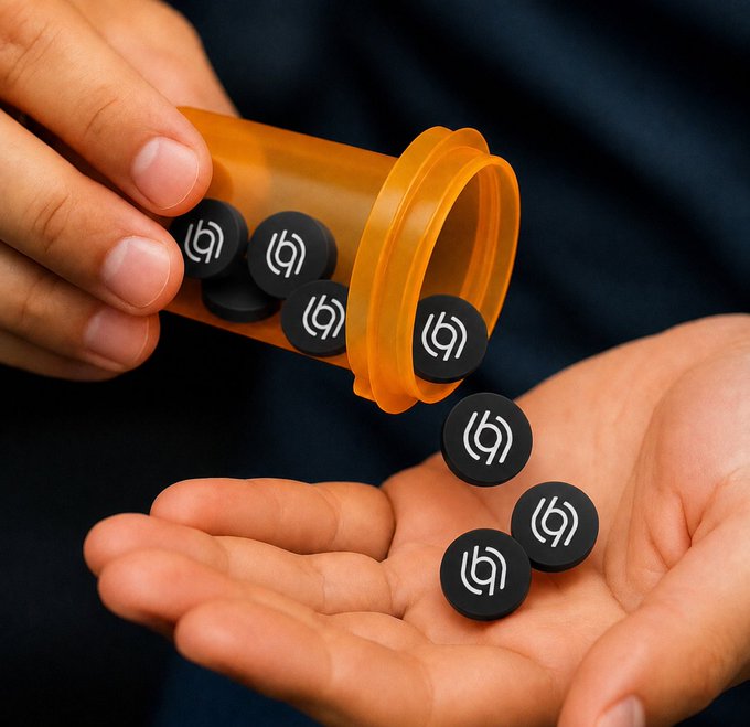 A hand pours black circular tokens featuring a spiral logo from an orange prescription bottle into an open palm.